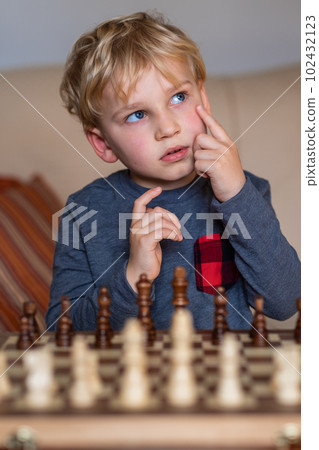 Small child 5 years old playing a game of chess on large chess board. Chess board on table in front of the boy thinking of next move Small child 5 years old playing a game of chess on large chess board. Chess board on table in front of the boy thinking of next move 102432123