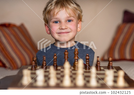 Small child 5 years old playing a game of chess on large chess board. Chess board on table in front of the boy thinking of next move Small child 5 years old playing a game of chess on large chess board. Chess board on table in front of the boy thinking of next move 102432125