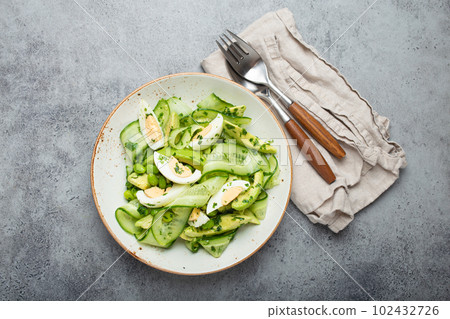 Healthy green avocado salad bowl with boiled eggs, sliced cucumbers, edamame beans, olive oil and herbs on ceramic plate top view, grey stone rustic table background Healthy green avocado salad bowl with boiled eggs, sliced cucumbers, edamame beans, olive oil and herbs on ceramic plate top view, grey stone rustic table background 102432726