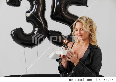 blonde woman in black with a cake with a candle number thirty-five 102432727
