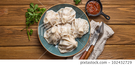 Georgian dumplings Khinkali on plate with red tomato sauce and fresh cilantro top view, rustic wooden background, traditional dish of Georgia 102432729