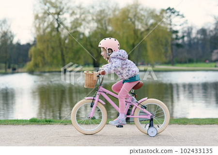 Girl riding bike in safe helmet at sunny spring park. Preschooler learning to balance on bicycle in safe helmet. Girl riding bike in safe helmet at sunny spring park. Preschooler learning to balance on bicycle in safe helmet. 102433135