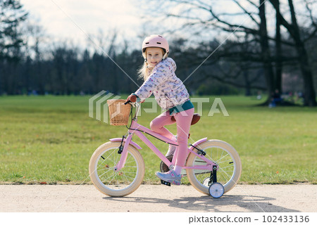 Girl riding bike in safe helmet at sunny spring park. Preschooler learning to balance on bicycle in safe helmet. Girl riding bike in safe helmet at sunny spring park. Preschooler learning to balance on bicycle in safe helmet. 102433136
