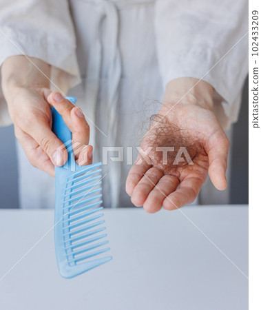 woman holds comb and fallen dark hair in hands. hair care, weak dull strands, home spa 102433209
