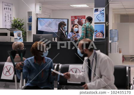 Female hospital staff members attending a sick young african american man at reception area. Doctor handing prescription to woman with partial body paralysis. Medical clinic lobby during covid Female hospital staff members attending a sick young african american man at reception area. Doctor handing prescription to woman with partial body paralysis. Medical clinic lobby during covid 102435170