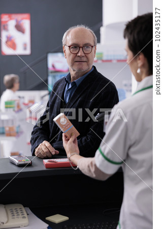 Old man in glasses waiting for drugstore cashier scanning product to pay. Young woman pharmaceutical worker using scanner on sunblock lotion barcode, selling medications to client 102435177