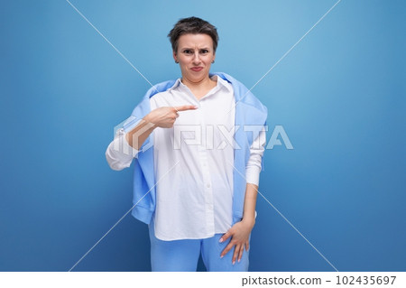 embarrassed young dark-haired woman with a short haircut in a white shirt points her finger to the 102435697