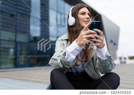 young attractive woman in the city listening to a podcast with headphones on the street 102435810