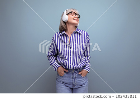 Energetic retired woman with gray hair masters headphone technique on a bright studio background Energetic retired woman with gray hair masters headphone technique on a bright studio background 102435811