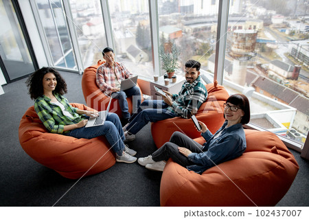 Males and females posing with gadgets in shared workspace 102437007