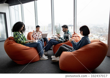 Multicultural teammates holding gadgets in coworking space 102437017