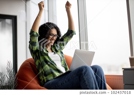 Female raising fists while reading email on laptop in office Female raising fists while reading email on laptop in office 102437018
