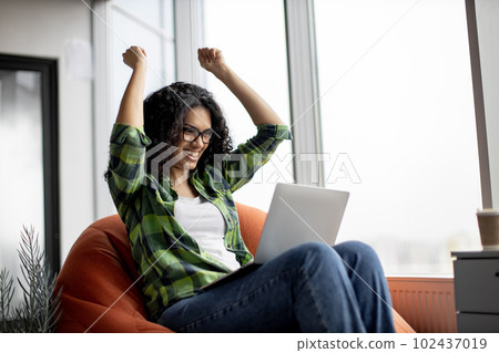 Female raising fists while reading email on laptop in office 102437019