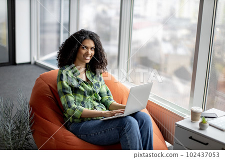 Businesswoman posing in beanbag with laptop at work Businesswoman posing in beanbag with laptop at work 102437053