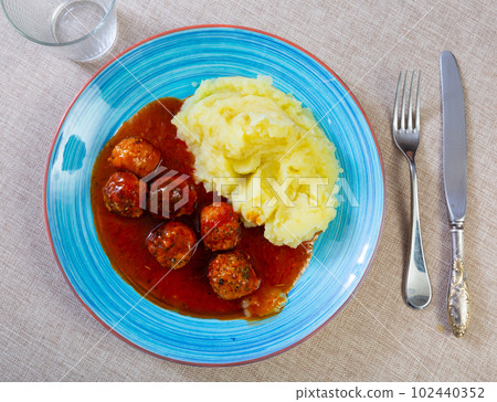 white round plate with meatballs sprinkled with chopped dill in tomato sauce with mashed potatoes 102440352