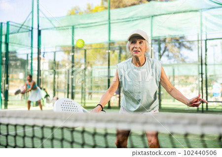 Active elderly woman playing padel tennis on open court Active elderly woman playing padel tennis on open court 102440506