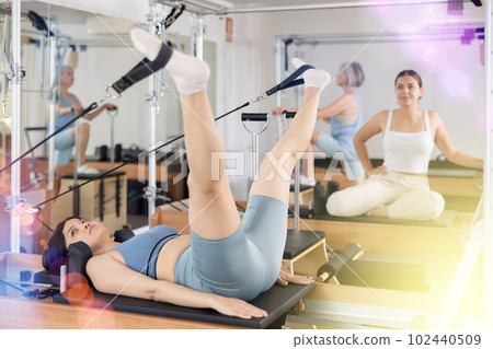 Woman exercising torson rotation at sport gym using pilates reformer beds Woman exercising torson rotation at sport gym using pilates reformer beds 102440509