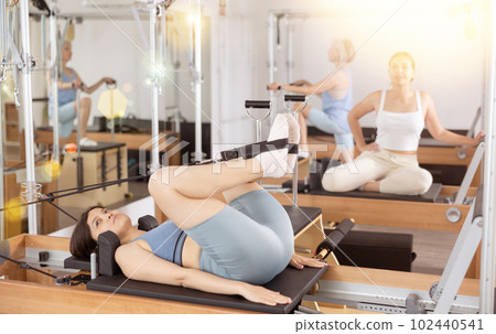 Positive woman practicing pilates stretching exercises on reformer at gym 102440541
