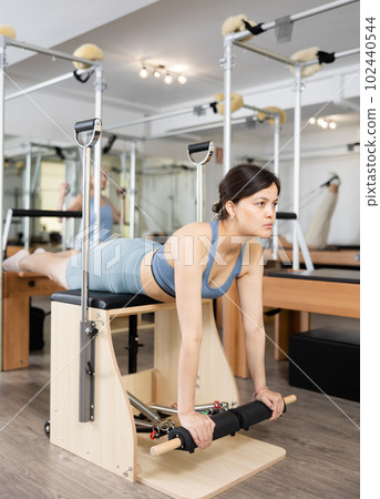 Young asian girl practicing pilates exercises on combo chair Young asian girl practicing pilates exercises on combo chair 102440544