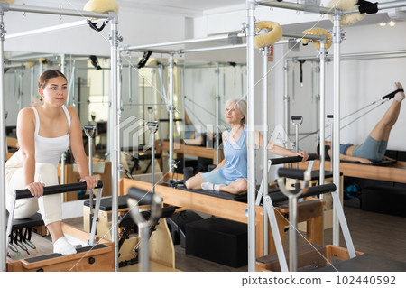 Positive young female in sportswear training twist rotation while using pilates performer bed in gym 102440592
