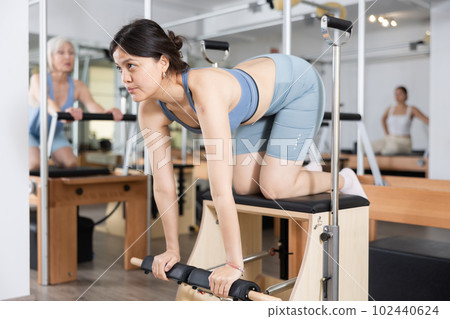 Young asian girl practicing pilates exercises on combo chair Young asian girl practicing pilates exercises on combo chair 102440624