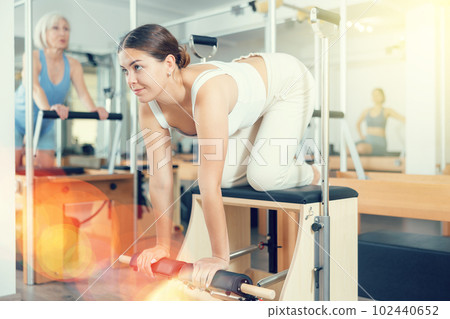 Young woman making pilates exercising while standing on knees using Wanda chair machine 102440652