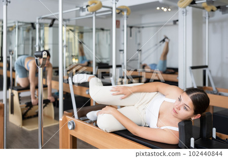 Young girl performing set of pilates exercises on reformer Young girl performing set of pilates exercises on reformer 102440844