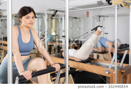 Young positive woman doing Pilates on special equipment in gym Young positive woman doing Pilates on special equipment in gym 102440854