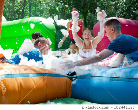 Cheerful girl with friends picking up balls in inflatable pool with foam 102441155