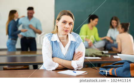 Upset girl sitting at table in auditorium during break on background with students 102441314