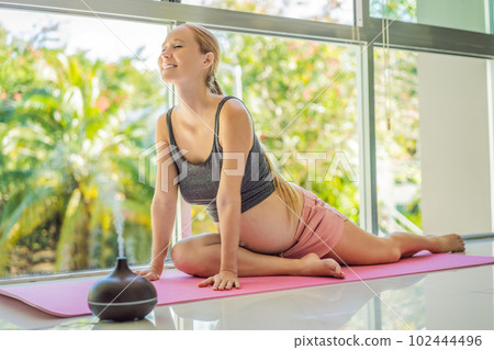 Young pregnant woman doing yoga exercises and meditating at home with an aroma diffuser. Health care, mindfulness, relaxation and wellness concept. Aromatherapy during pregnancy Young pregnant woman doing yoga exercises and meditating at home with an aroma diffuser. Health care, mindfulness, relaxation and wellness concept. Aromatherapy during pregnancy 102444496