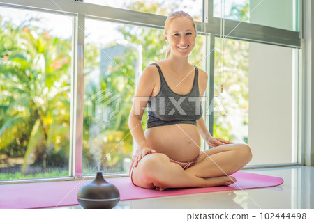 Young pregnant woman doing yoga exercises and meditating at home with an aroma diffuser. Health care, mindfulness, relaxation and wellness concept. Aromatherapy during pregnancy 102444498