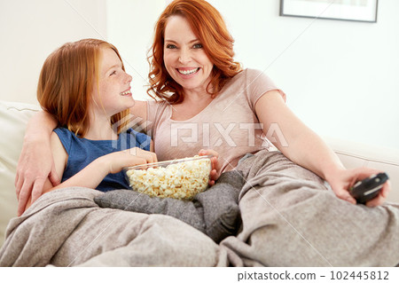 She picked tonights movie. a mature woman and her young daughter watching a movie and eating popcorn on the sofa. 102445812