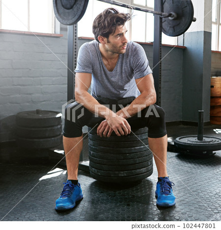 That was a heck of a workout. a young man taking a break from working out with weights in the gym. That was a heck of a workout. a young man taking a break from working out with weights in the gym. 102447801