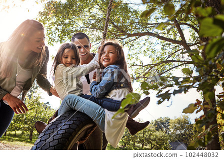 Making family memories. a happy mother and father pushing their daughters on a tyre swing. Making family memories. a happy mother and father pushing their daughters on a tyre swing. 102448032