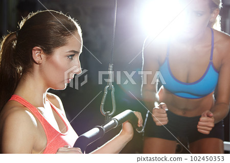 Only one more set to go. a young woman working out at the gym with her friend encouraging her. Only one more set to go. a young woman working out at the gym with her friend encouraging her. 102450353