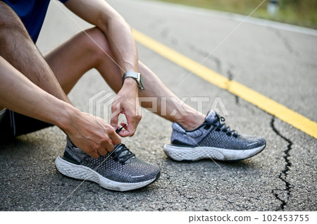 A man sits on street and tying his sport shoes laces, preparing for running 102453755