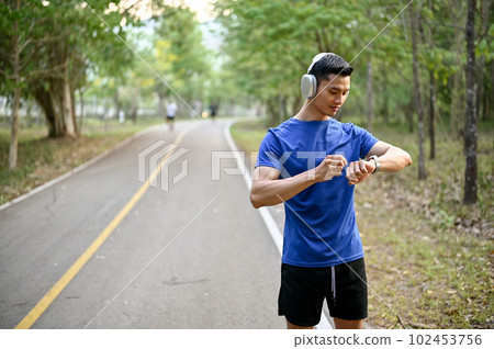 Handsome Asian man wearing headphones, checking his running miles on his smartwatch 102453756
