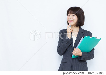 A woman in her thirties in a suit thinking with a smile in front of a white background 102455488