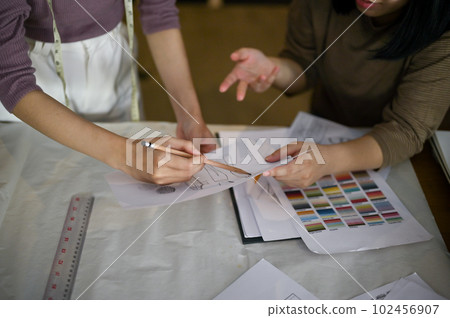 Two professional female dressmakers checking new model sketches in the studio together. 102456907