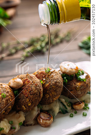 Pouring olive oil on falafels with mushrooms Pouring olive oil on falafels with mushrooms 102457130