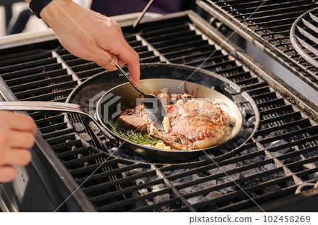 Male chef preparing T-bone steak on carbon steel frying pan outdoor on grill. BBQ concept. Close-up 102458269