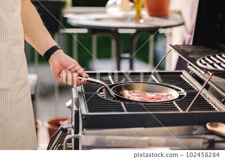 Man hold pan on hot coal on grill. Grilling beef steak on carbon steel pan. Side view Man hold pan on hot coal on grill. Grilling beef steak on carbon steel pan. Side view 102458284