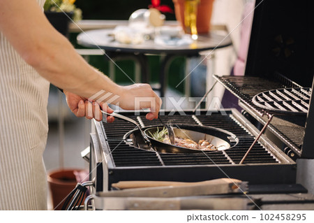 Side view of male chef preparing T-bone steak on frying pan. Classic version of cocking beef. Rosemary and butter 102458295