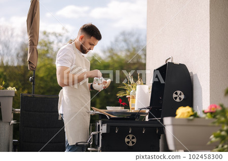 Man salted food in frying pan and prepare meal outdoor on BBQ grill 102458300