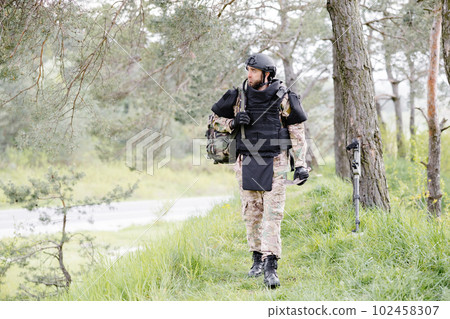 Young soldier in uniforms and tactical vest works in the forest and prepares for action at a temporary forest base. A man does in the work of demining the territory Young soldier in uniforms and tactical vest works in the forest and prepares for action at a temporary forest base. A man does in the work of demining the territory 102458307