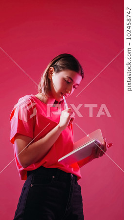 Think idea. Making checklist. Inspired student. Pensive girl writing paper notebook thoughtful expression to do list planning isolated on neon color pink background. 102458747