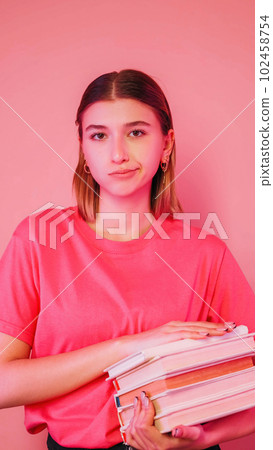 Dissatisfied student. Reading books. Preparing exam. Pretty frustrated girl holding textbooks displeased expression isolated on neon color pink background. 102458754