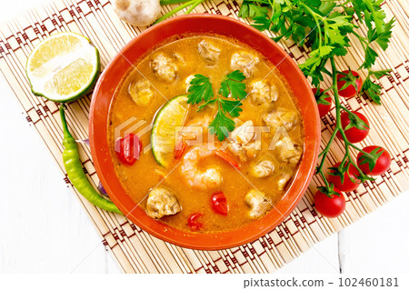 Soup Tom Yum with lime in bowl on light board top 102460181