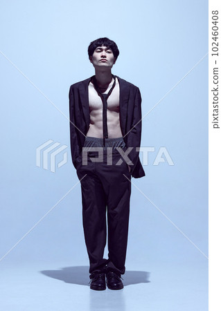 Portrait of young stylish man posing in black jacket on naked body with tie and classical pants against light blue studio background 102460408